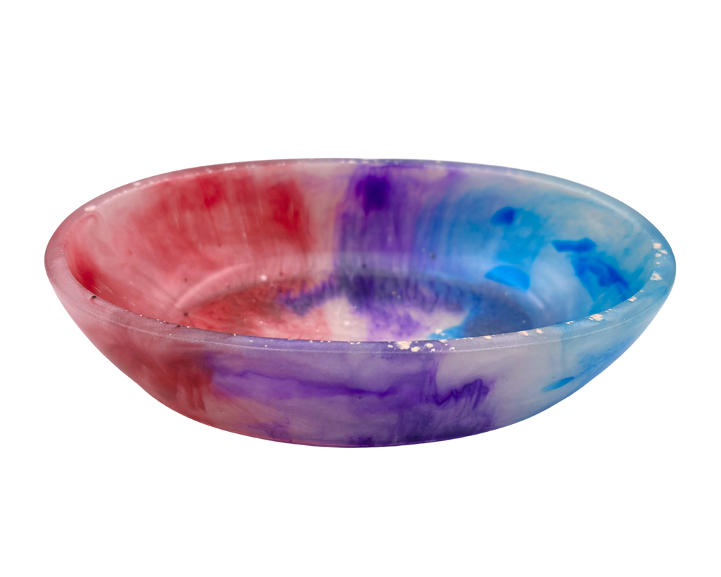 A shallow round resin bowl featuring a marbled tie-dye pattern of pink, purple, and blue on a white base, isolated on a white background.