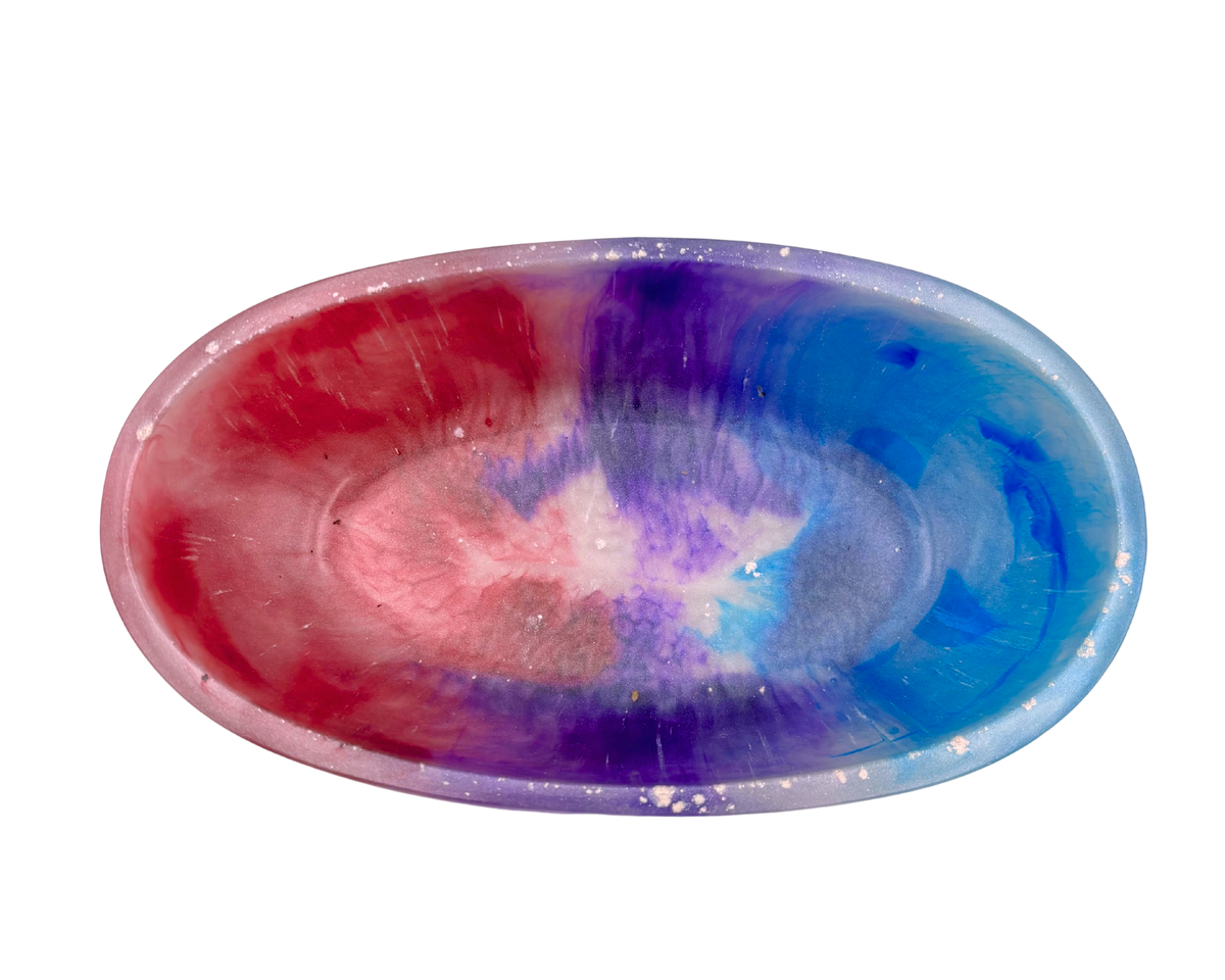 A shallow round resin bowl featuring a marbled tie-dye pattern of pink, purple, and blue on a white base, isolated on a white background.