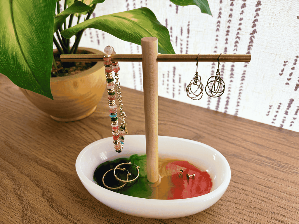 White resin tray with multicolored bottom with wooden and brass jewelry holder with earrings and bracelets on table
