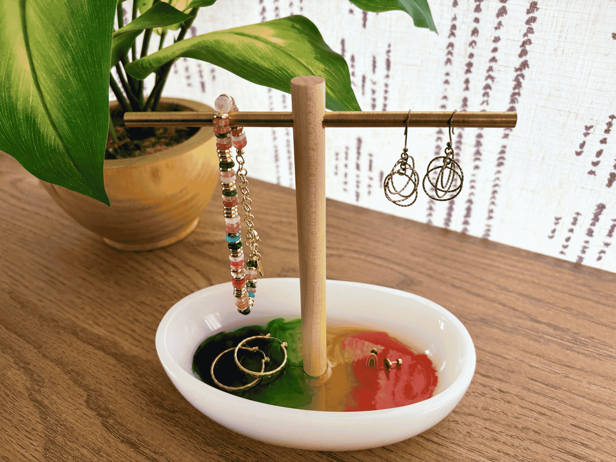 White resin tray with multicolored bottom with wooden and brass jewelry holder with earrings and bracelets on table
