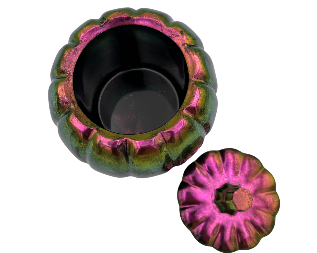 A small pumpkin-shaped container with a matching lid, shown on a plain white background. The container has a metallic iridescent finish shifting between green, gold, and magenta-pink, with a black interior.