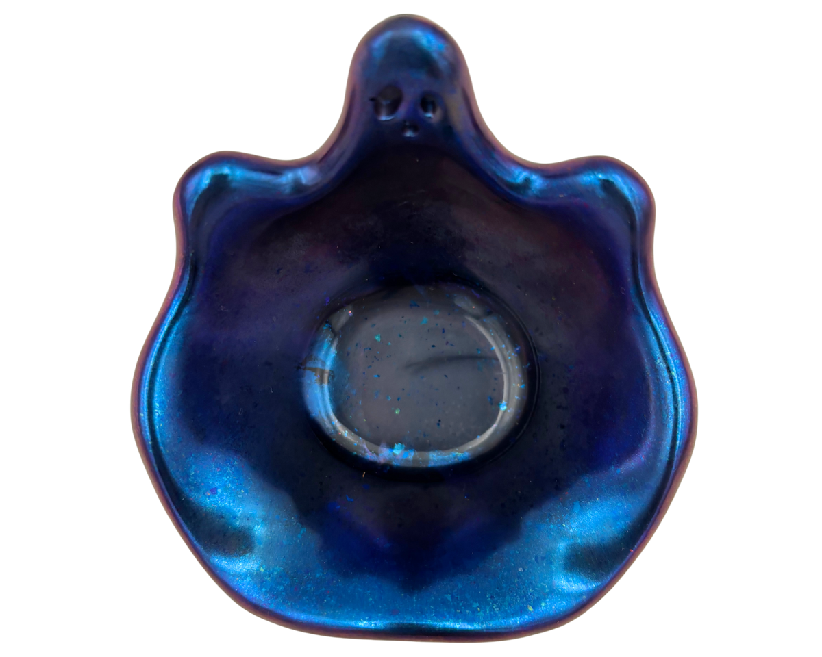 A small ghost-shaped resin bowl with a skull face, featuring a deep blue and purple iridescent glaze with subtle glitter, set against a plain white background.