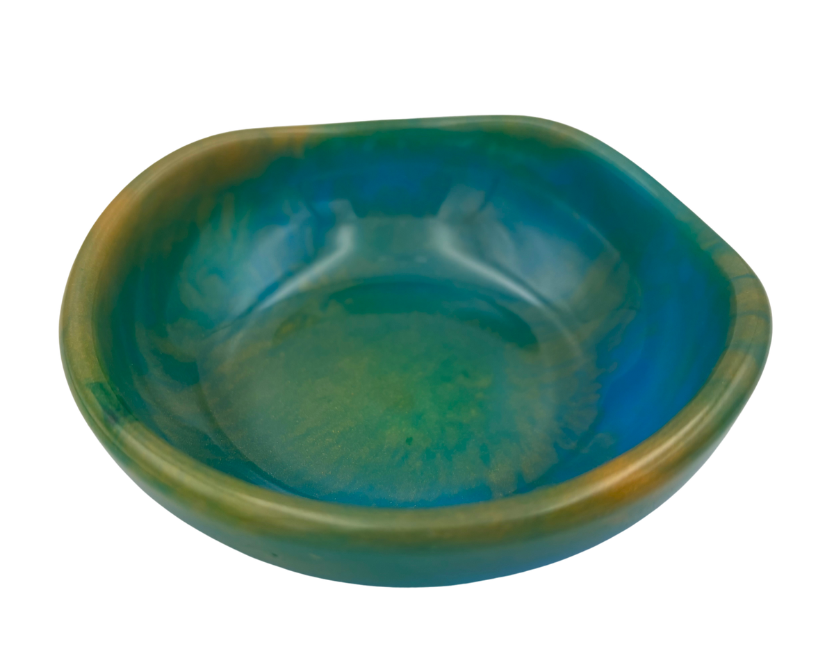 A small resin bowl with a rounded, organic shape, featuring a glossy glaze that transitions from deep teal-blue to olive green and mustard-gold around the rim, shown on a plain white background.