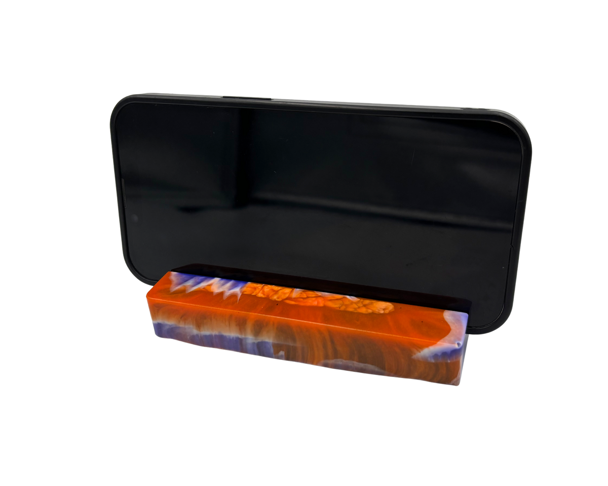 A mobile phone stand holding a phone, featuring a marbled pattern of vibrant orange, deep blue, and white swirls with a textured bubbly finish.