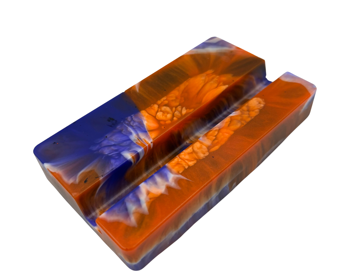 A mobile phone stand, featuring a marbled pattern of vibrant orange, deep blue, and white swirls with a textured bubbly finish.