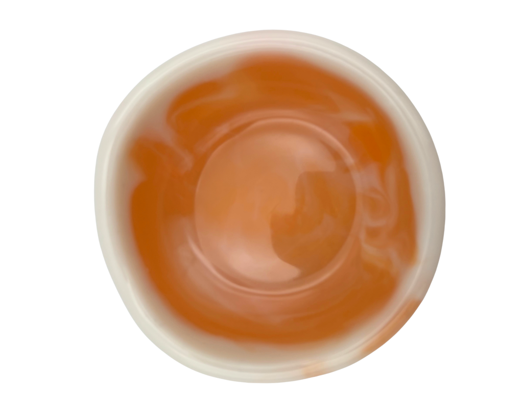 A top-down view of a small, round, off-white resin dish with orange swirls, isolated on a solid white background.