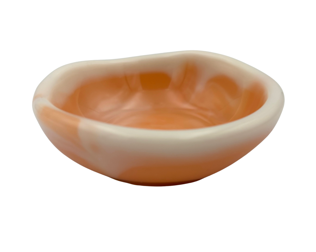 A side view of a small, round, off-white resin dish with orange swirls, isolated on a solid white background.