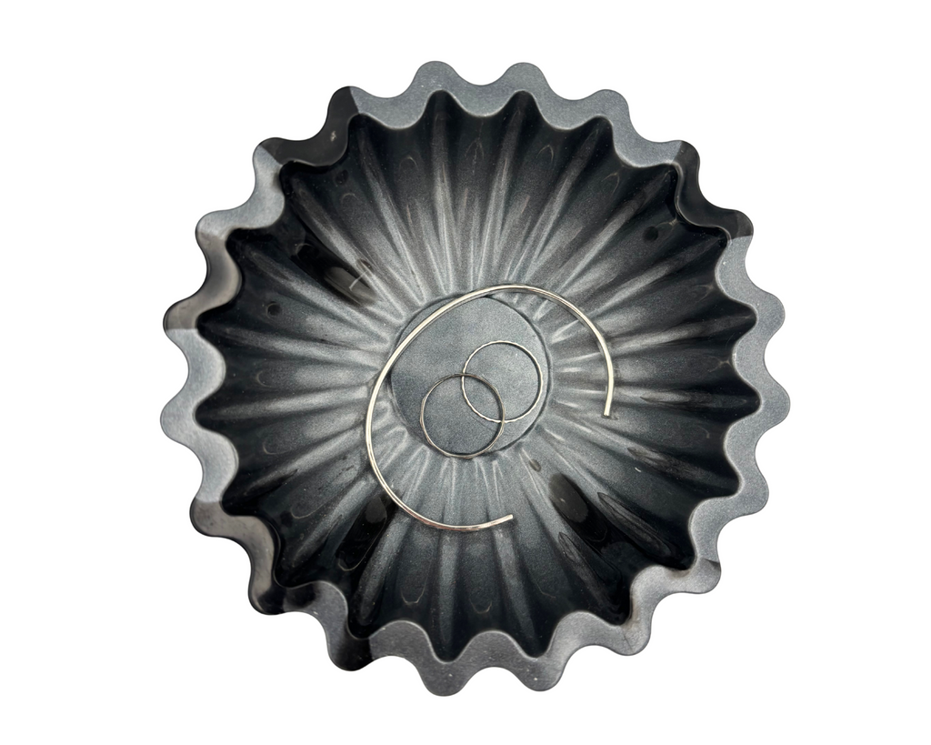 Gray and black resin bowl with scalloped edges holding jewelry