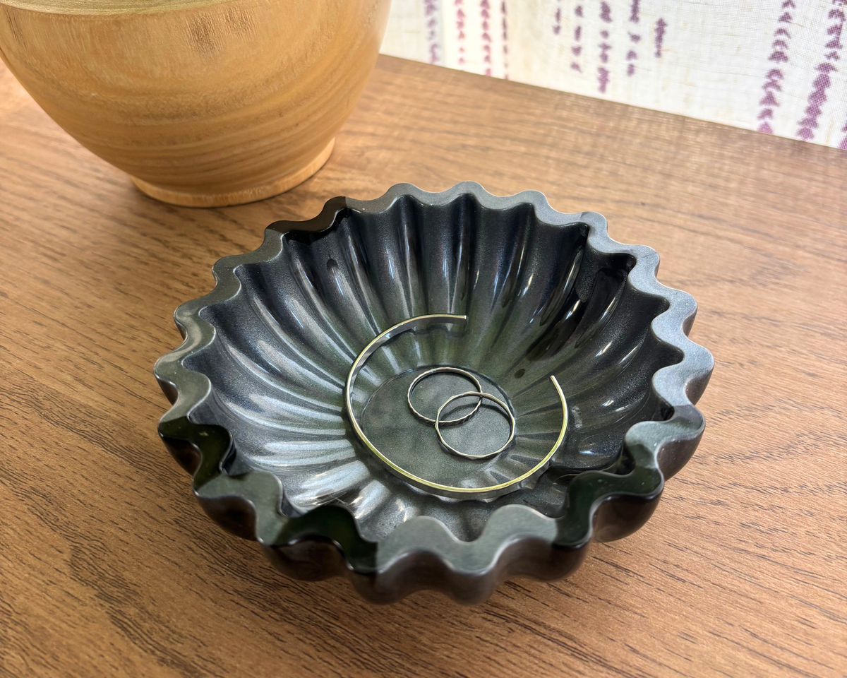 Gray and black resin bowl with scalloped edges holding jewelry