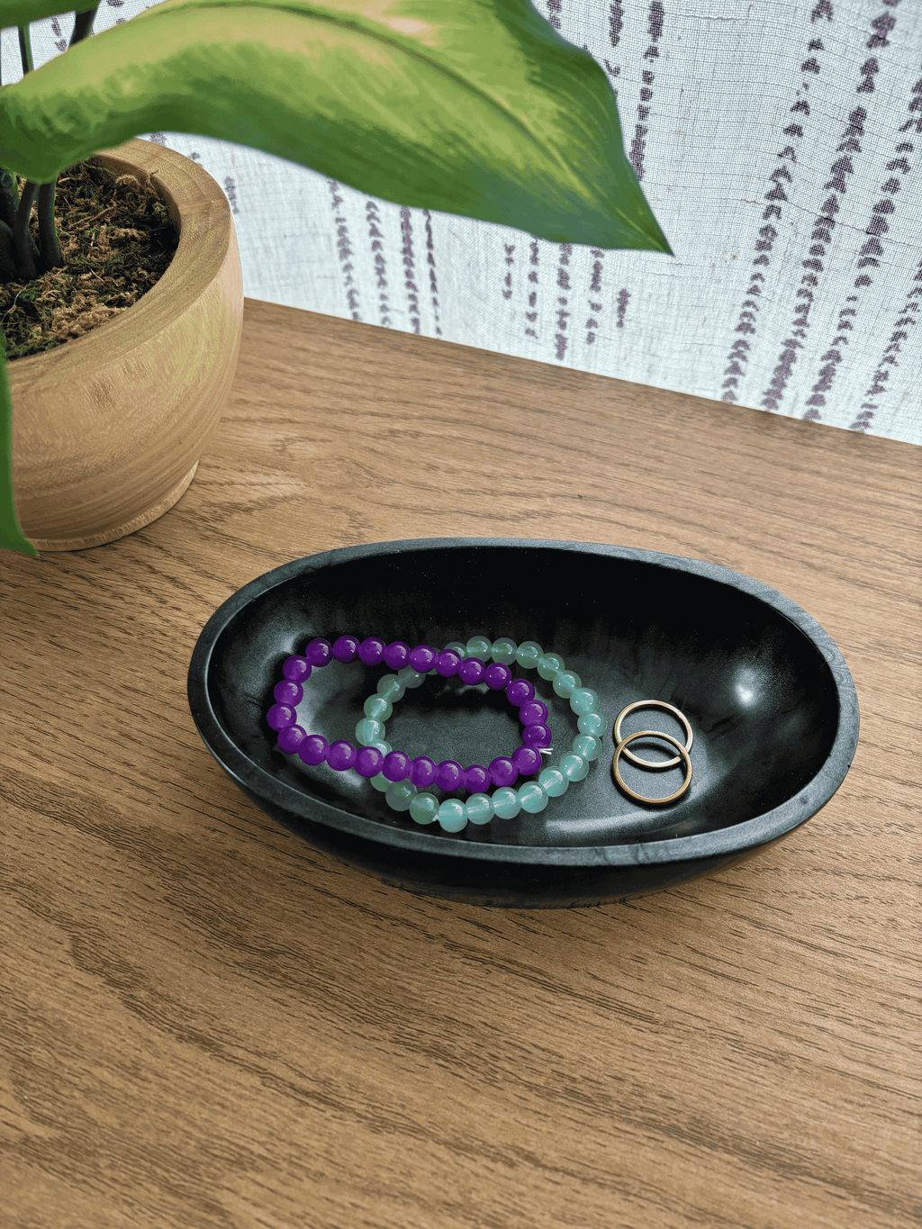 Black and gray oval resin dish holding bracelets and rings on wooden table