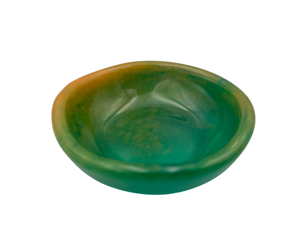 A small, shallow oval dish or bowl made of green resin with a warm amber-orange tint along the upper left edge, shown on a plain white background.