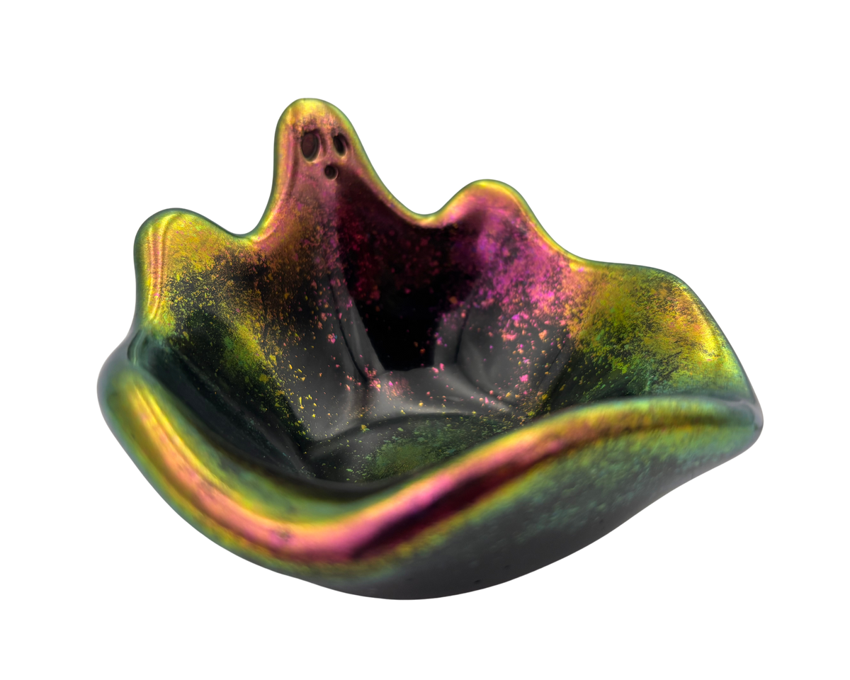 A small decorative bowl with a ghost-shaped silhouette, featuring an iridescent finish that shifts between green, gold, pink, and purple, with fine glitter inside.