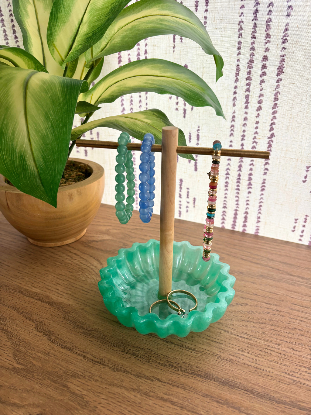 Green resin tray with wooden and brass jewelry holder with bracelets and earrings on wooden table