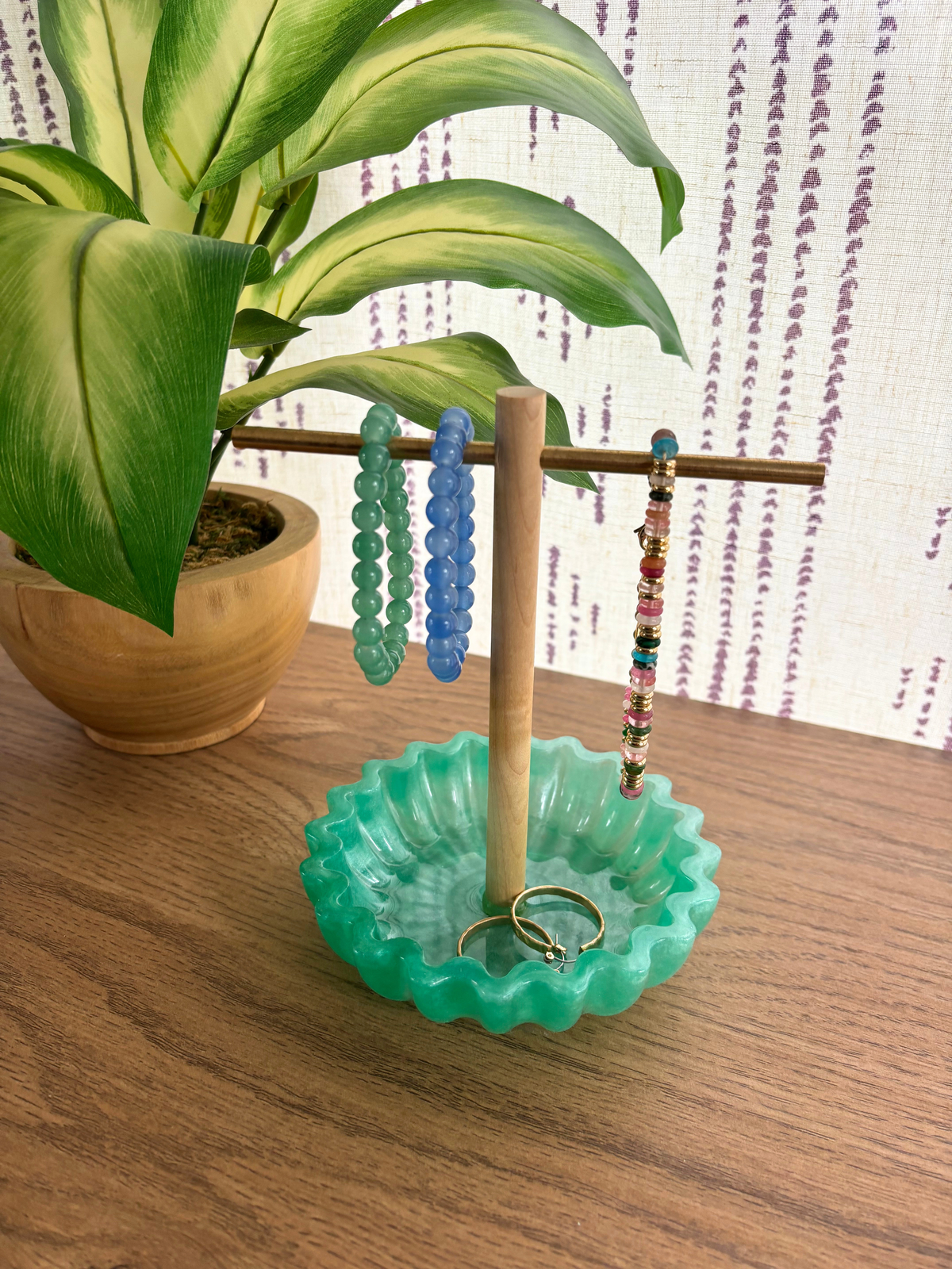Green resin tray with wooden and brass jewelry holder with bracelets and earrings on wooden table