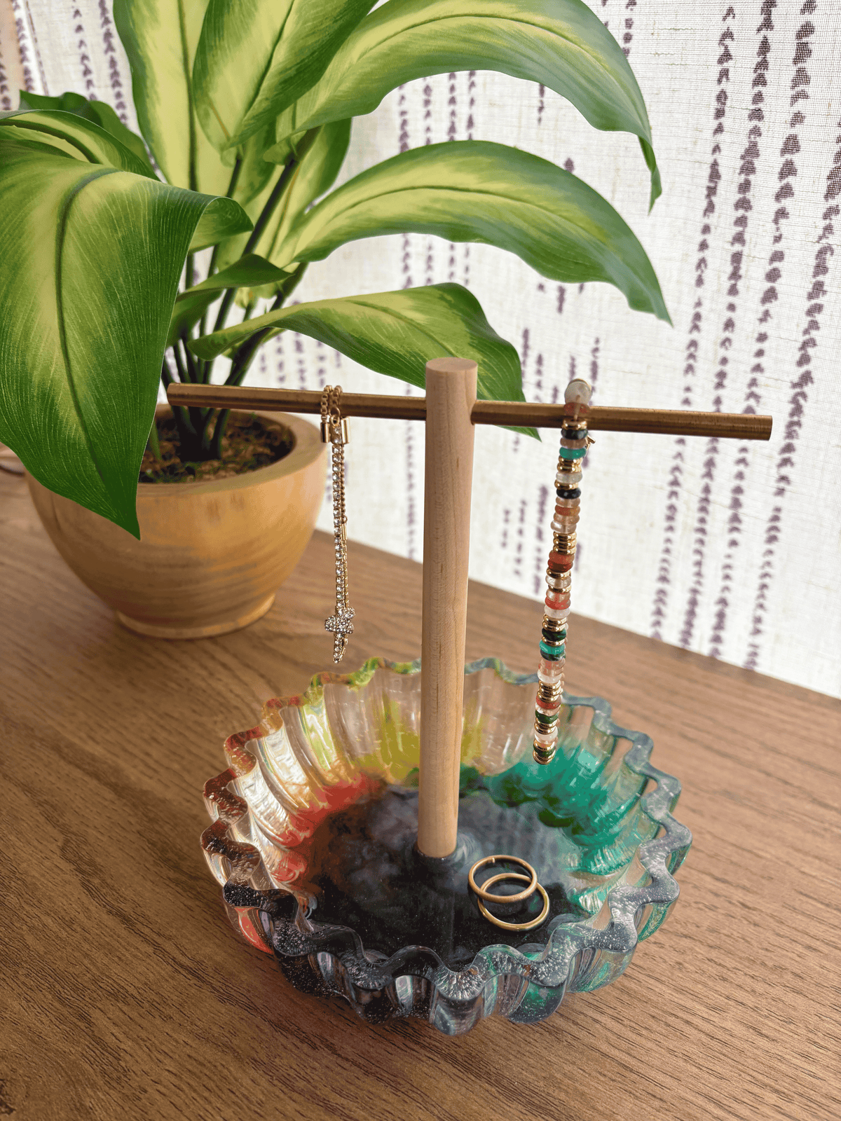 Colorful resin bowl with a wooden and brass jewelry tree holding bracelets and rings on a table