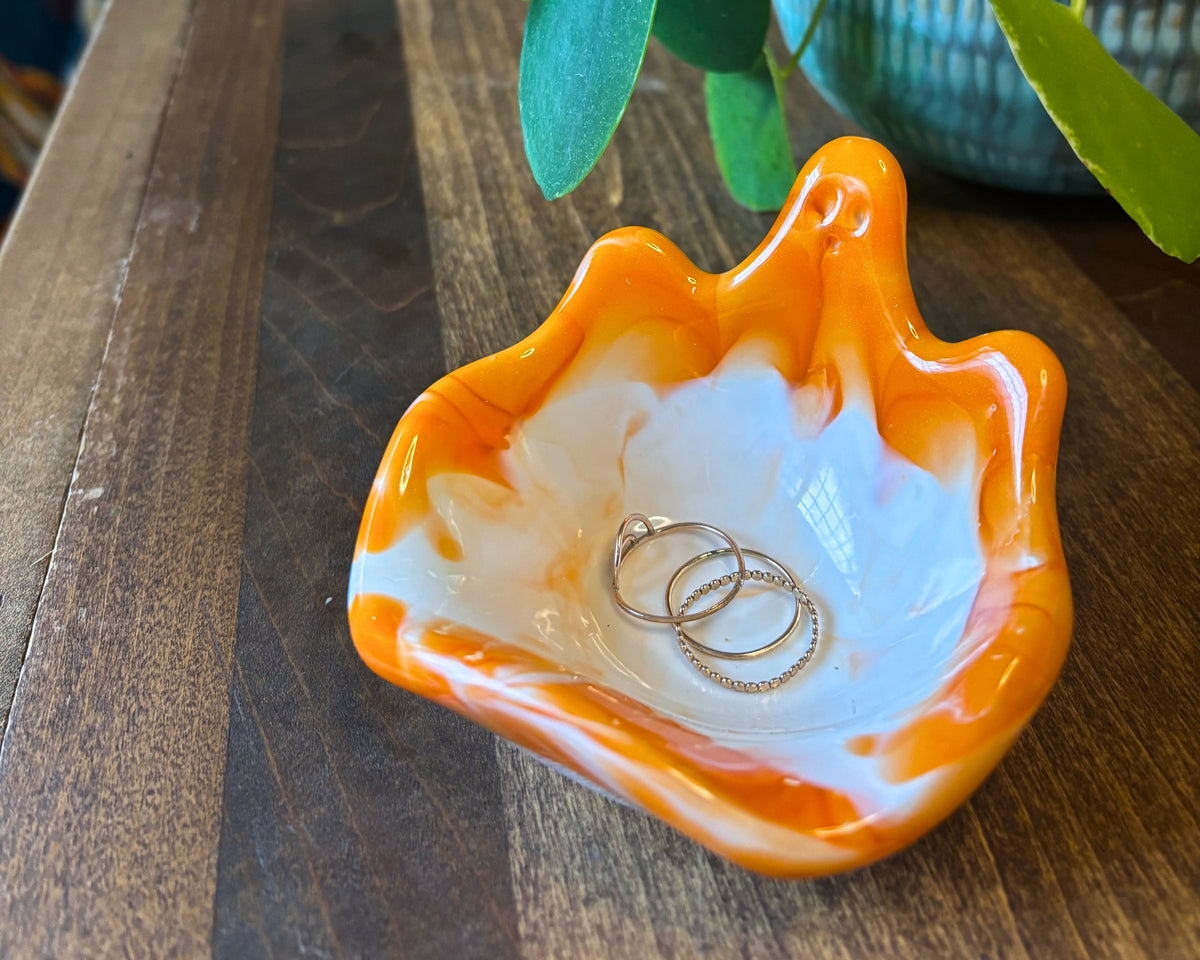 An orange and white marbled resin bowl with a ghost silhouette, photographed on a wooden table with a plant.