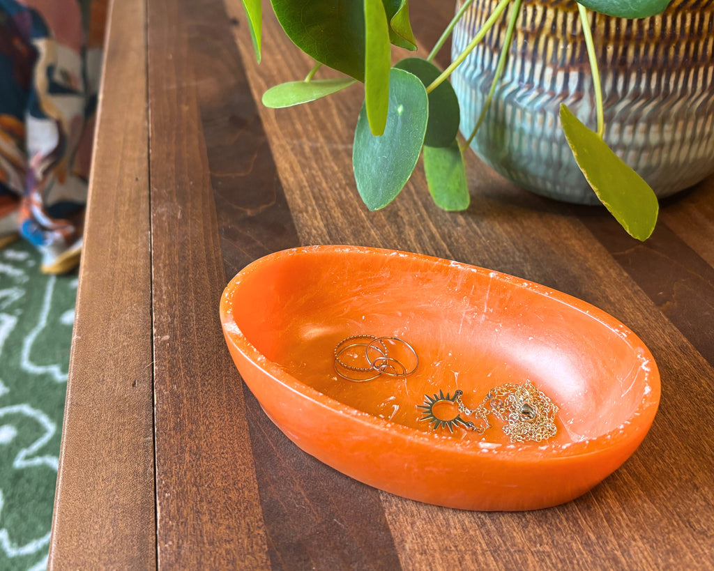 An orange resin bowl with a shallow depth, shown from a top-down perspective on a table with a plant