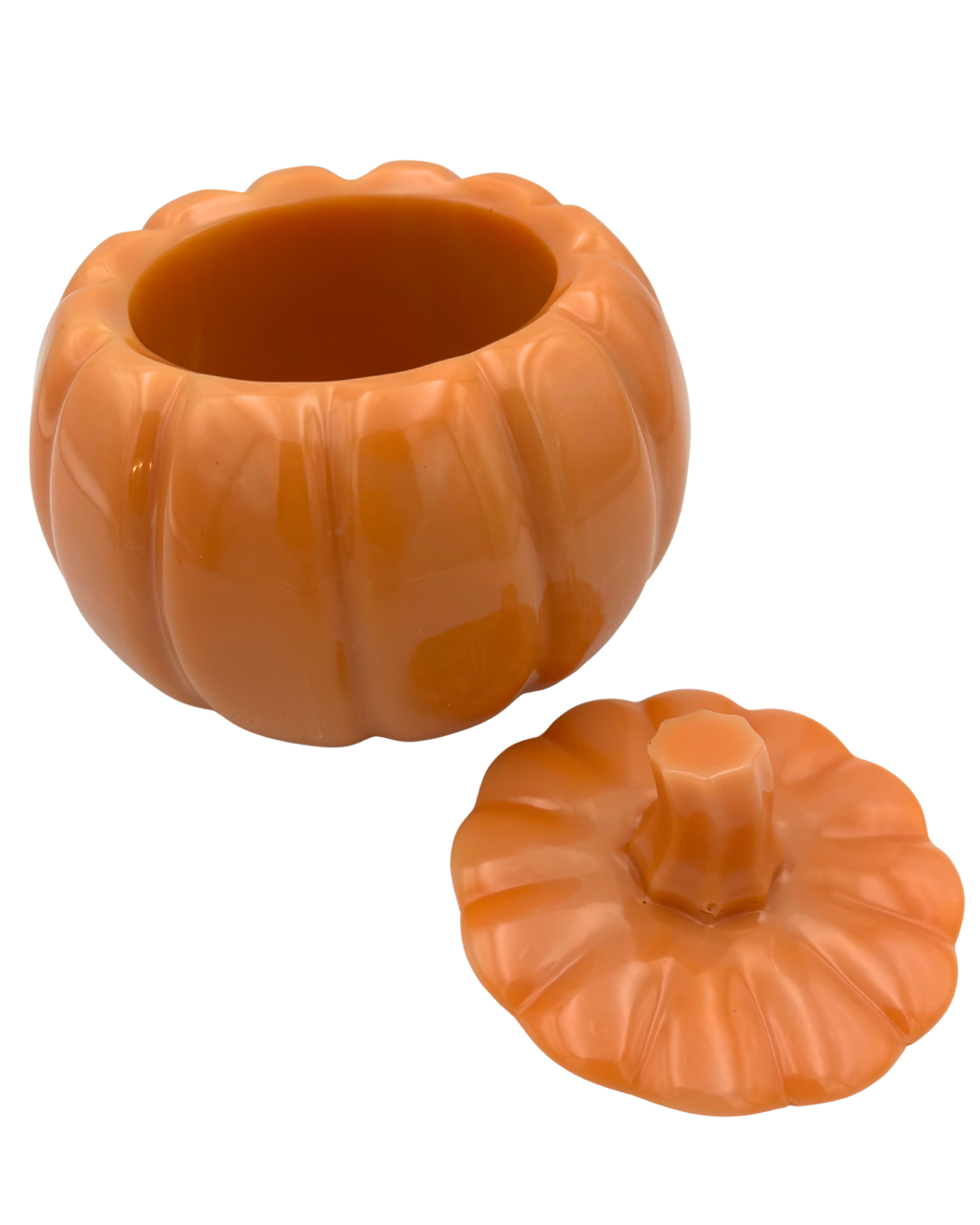 An orange pumpkin-shaped container with its lid placed beside it on a plain white background.