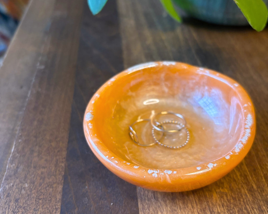 An orange resin ring dish, photographed from a top-down angle on a wooden table
