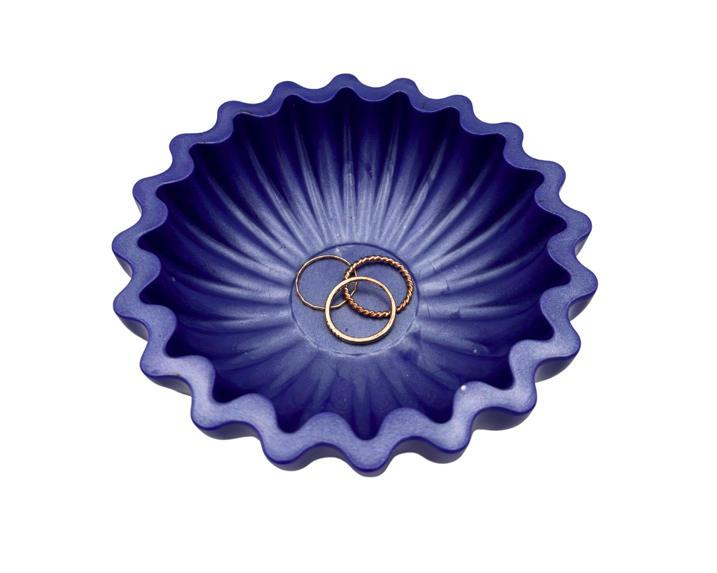 A small scalloped resin bowl in a deep periwinkle, containing rings, set against a plain white background.