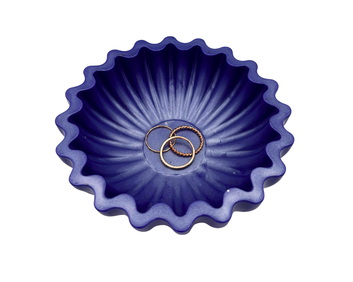 A small scalloped resin bowl in a deep periwinkle, containing rings, set against a plain white background.