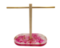 A jewelry display stand with a rectangular pink and white marbled resin base containing small gold flakes, a vertical wooden rod, and a horizontal gold metal bar, shown on a plain white background.