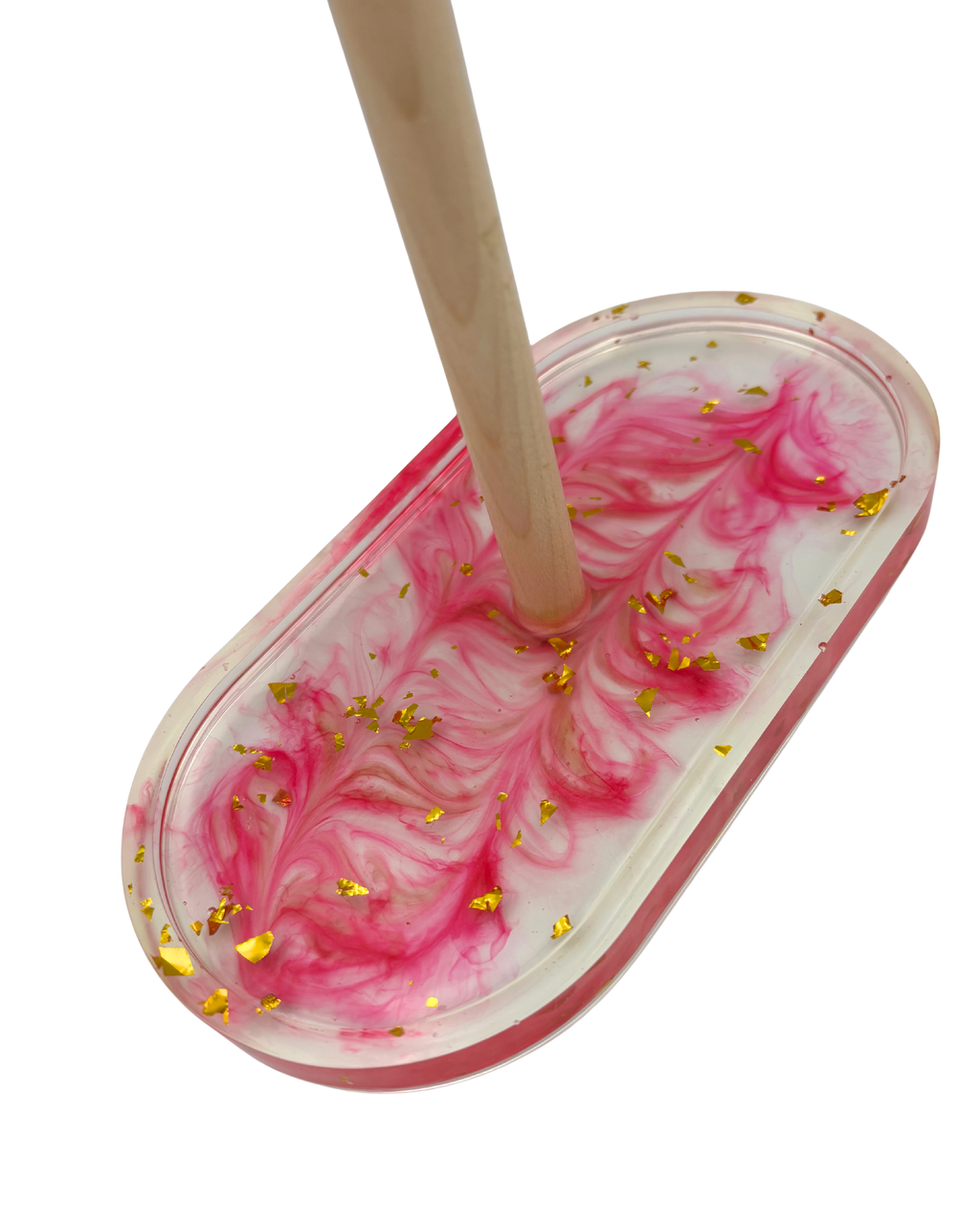 An oval resin tray with a wooden rod, filled with pink and white marbled resin and decorated with scattered gold foil flakes, shown on a plain white background.