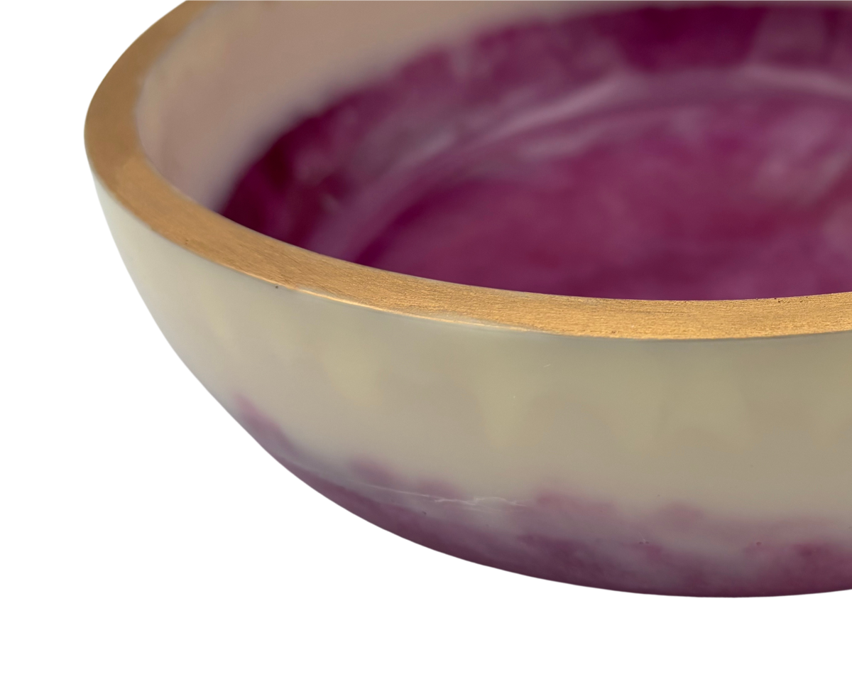 A close-up of a handcrafted bowl with a gold finish, featuring a cream-colored exterior, a purple marbled interior.