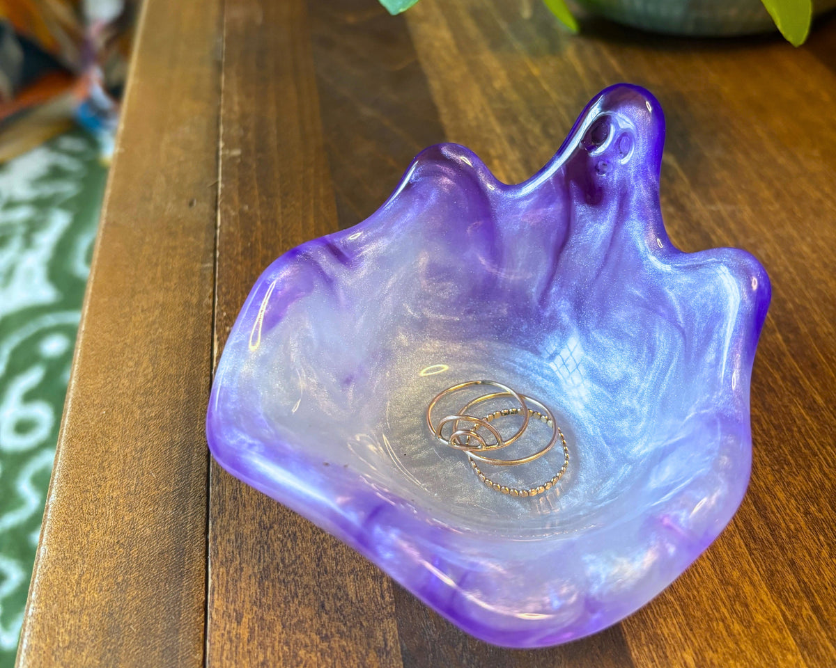 A purple and lavender iridescent resin dish with a wavy, organic shape, resting on a wooden table with green plant leaves in the background.