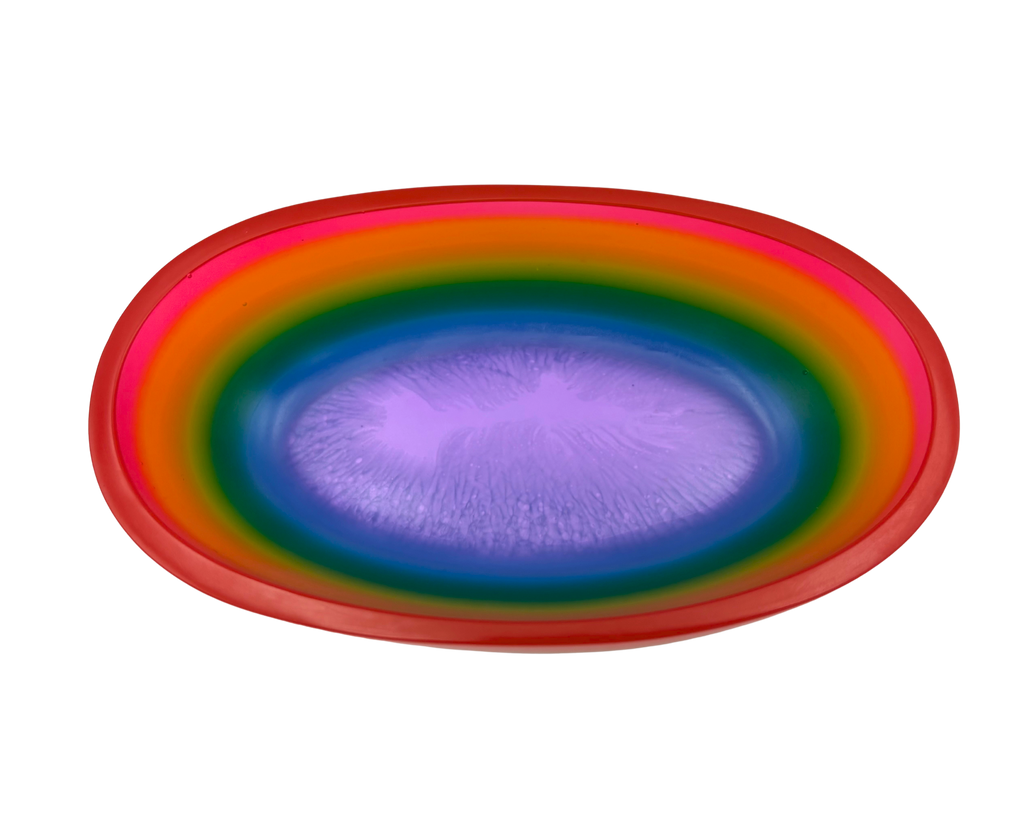 A shallow oval resin bowl with a vibrant rainbow gradient design, featuring concentric bands of red, orange, yellow, green, blue, and purple on a plain white background.
