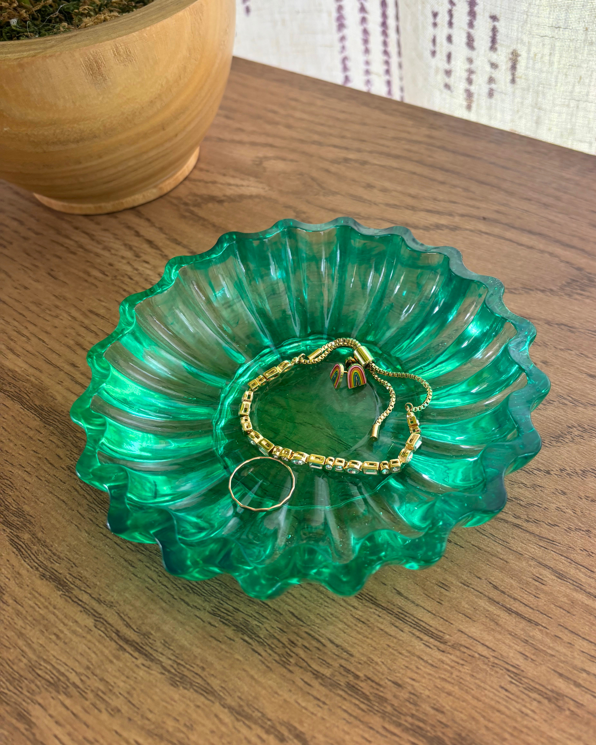 Green resin bowl with scalloped edges holding jewelry on a table