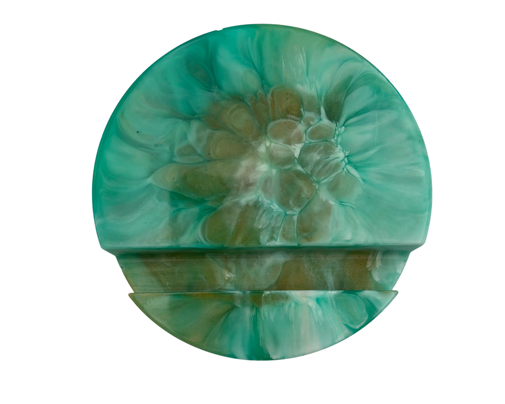 a round phone stand made of resin with teal and bronze patterns, on a white background