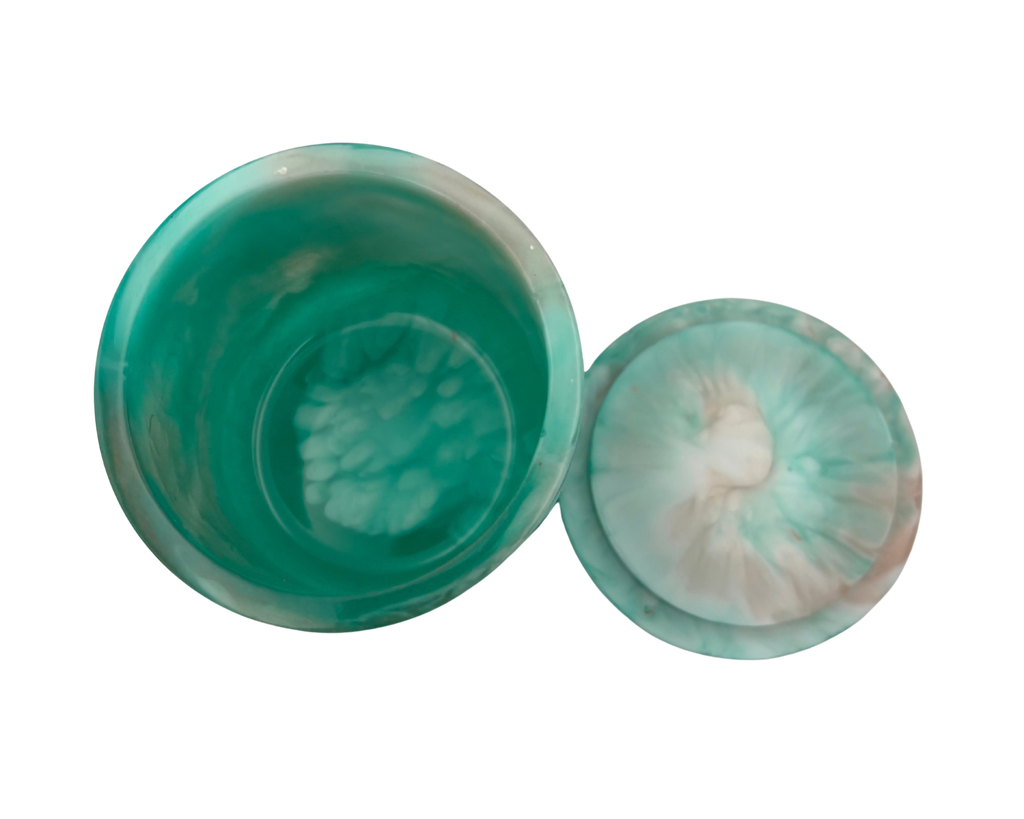 A cylindrical resin jar with a marbled green and white design, featuring a solid teal-green base and a swirled white and light teal lid.